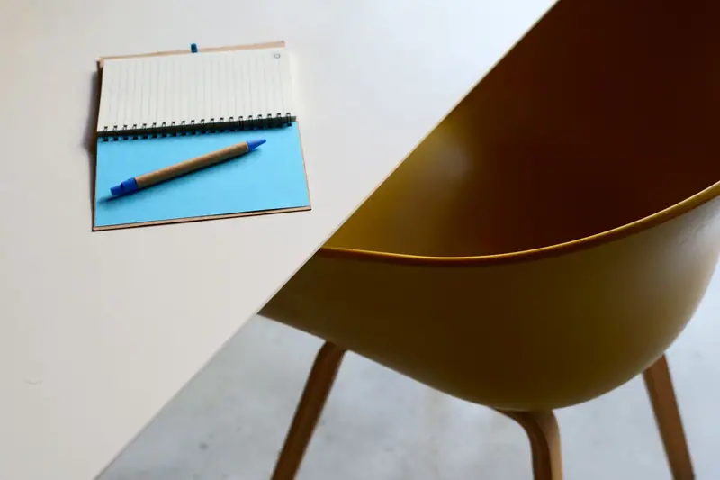 Lyst og ryddig skrivebord med notatbok og en gul stol
